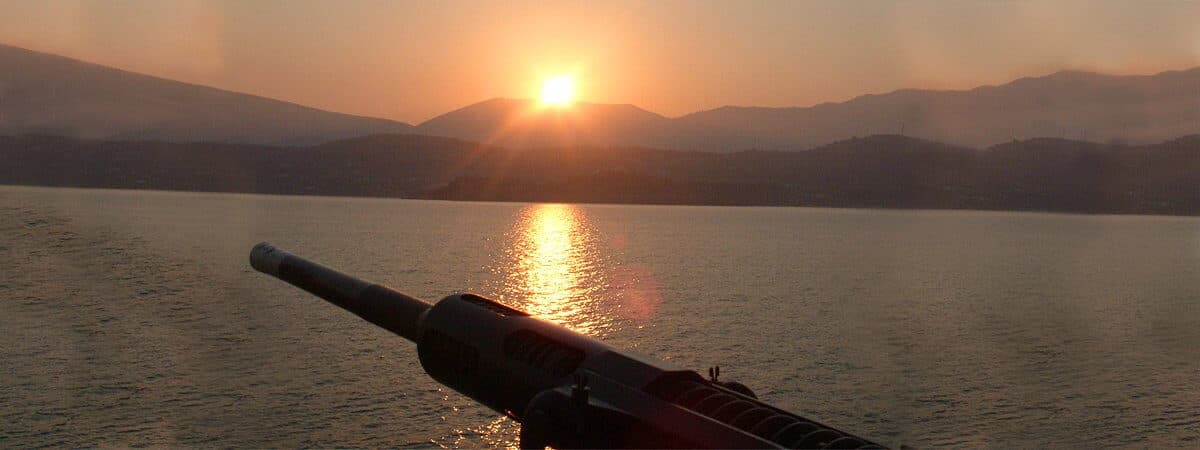 Deck gun of a naval vessel pointing toward the sunset over the Haifa coastline