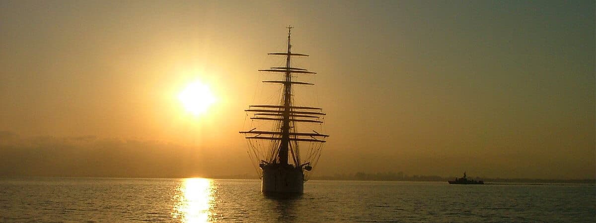 Tall ship silhouetted against the setting sun at sea